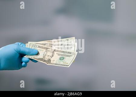 men's hand in medical gloves with a bunch of dollar bills Stock Photo