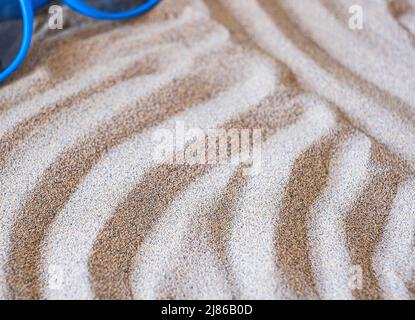 Wavy sea sand and blue sunglasses background. Flat lay. Copy space Stock Photo