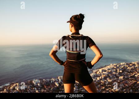 Rear view of sportswoman looking at the view from top. Female with her hands on hips enjoying a view. Stock Photo