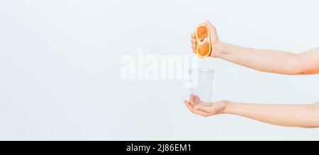 Female hands squeezing juice from fresh grapefruit into glass on white background Stock Photo
