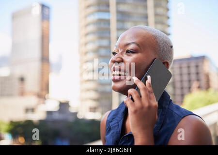 An attractive Black businesswoman laughs on a call on the office balcony Stock Photo