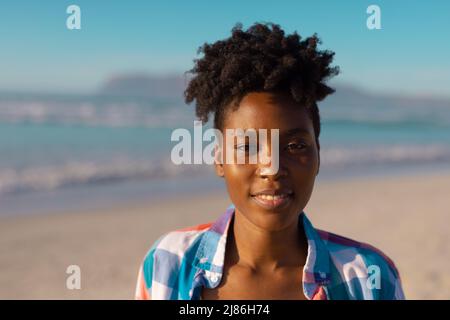 Portrait of smiling african american young woman with short curly hair at beach against clear sky Stock Photo