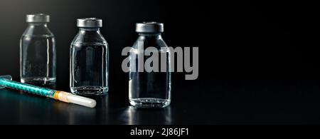 Three clear vaccine bottles with no labels on black background green hypodermic syringe near, space for text right side Stock Photo