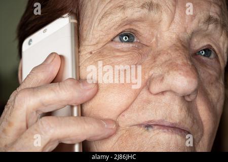 Elderly senior woman holding gold coloured phone next to her ear, closeup detail Stock Photo