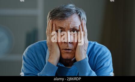 Depressed frustrated old senior Caucasian man shocked sad elderly mature 60s male feeling worried looking at camera holding head stressed businessman Stock Photo