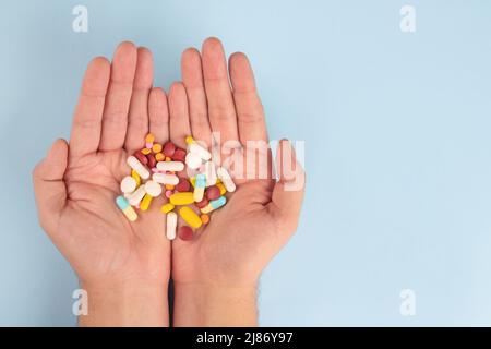 Man holding variety of medicine pills, capsules and tablets in his hands against blue background with copy space. Immune system vitamins and supplemet Stock Photo