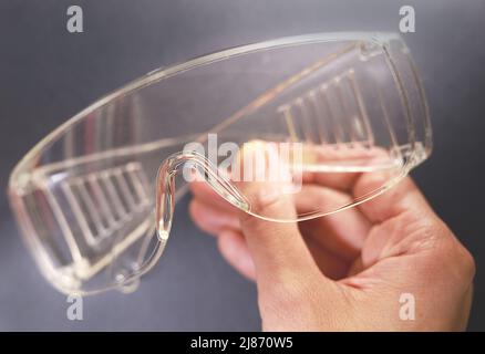 Protective glasses in hand, healthcare and safety concept. Safety glasses on black background. Personal protective equipment. Plastic goggles. Stock Photo