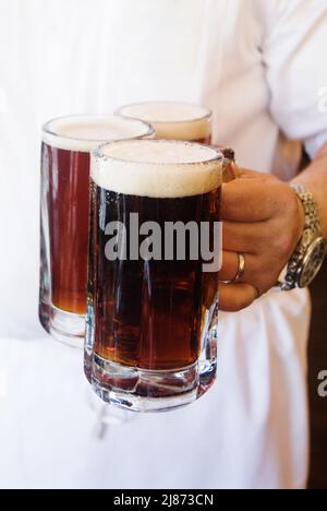 Hand holding three mugs of beer Stock Photo