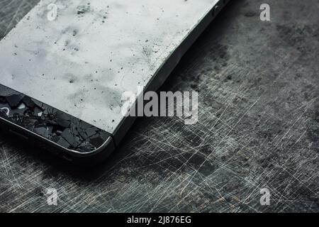 Badly damaged smartphone with bent metal case and broken glass on grunge background. Close-up. Stock Photo