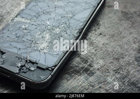 Badly damaged smartphone with bent metal case and broken glass on grunge background. Close-up. Stock Photo