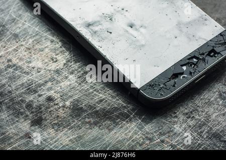 Badly damaged smartphone with bent metal case and broken glass on grunge background. Close-up. Stock Photo