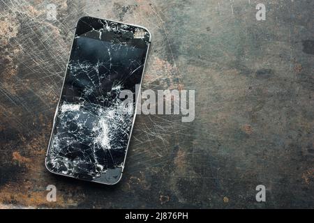 Badly damaged smartphone with bent metal case and broken glass on grunge background. Close-up. Stock Photo