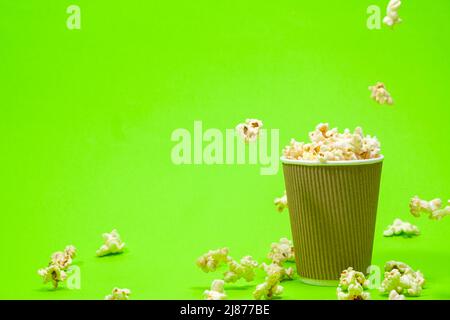 Popcorn is poured into a paper brown glass on a green background with place for text. Stock Photo