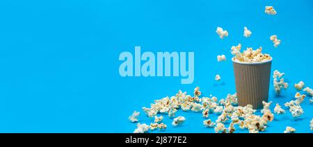 Popcorn is poured into a paper brown glass on a blue background with place for text. Stock Photo