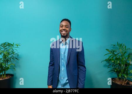 Portrait of smiling young african american businessman standing against blue wall at workplace Stock Photo