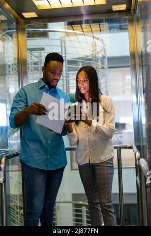 Young multiracial business colleagues discussing over document in elevator at modern workplace Stock Photo