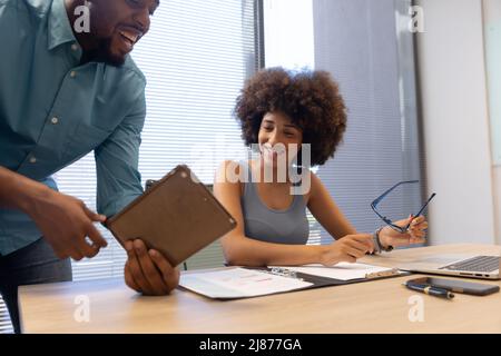Happy biracial business colleagues discussing over digital tablet in modern workplace Stock Photo
