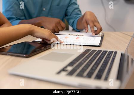 Midsection of biracial male and female colleagues discussing over document at desk in workplace Stock Photo