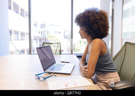 Side view of young hispanic businesswoman sitting with laptop at desk in modern workplace Stock Photo