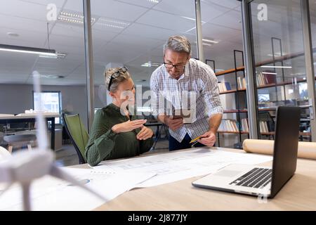 Smiling caucasian engineering colleagues discussing together over blueprint at modern workplace Stock Photo