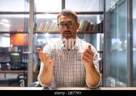 Portrait of confident businessman gesturing while sitting at desk in modern workplace Stock Photo