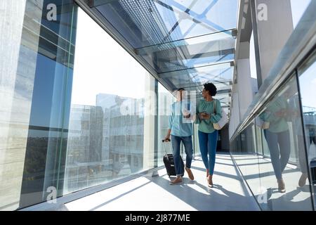 Young african american male and female colleagues walking with luggage at airport corridor Stock Photo