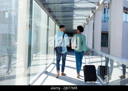 Rear view of african american business colleagues discussing while walking with luggage in airport Stock Photo