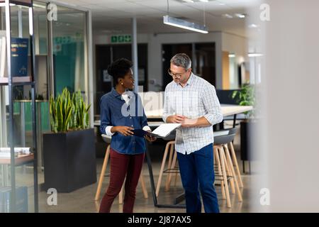 Biracial male and female professionals discussing over file while standing together at workplace Stock Photo