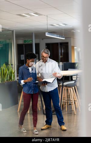 Full length of multiracial male and female professionals discussing over file at modern workplace Stock Photo