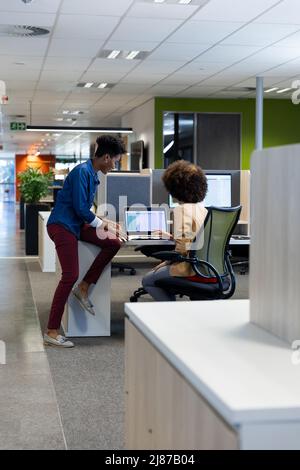 Young multiracial female professionals planning while discussing over laptop in cubicle at workplace Stock Photo