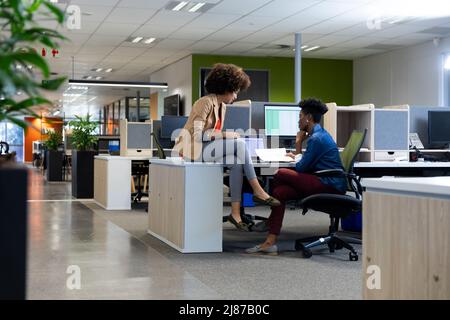 Young multiracial female colleagues discussing over document sitting together in cubicle Stock Photo