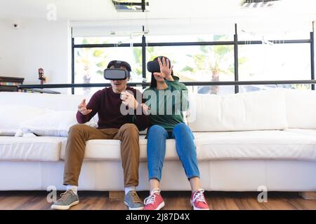 Excited young asian couple using virtual reality while gesturing on couch in living room at home Stock Photo