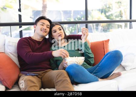 Romantic young asian couple watching tv while eating popcorn on couch at home Stock Photo