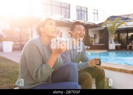 Cheerful young asian couple having coffee while relaxing outside house during sunny day Stock Photo