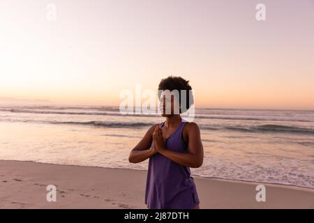 African american mature woman with afro hair meditating while standing at beach against clear sky Stock Photo