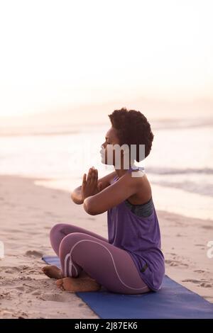 Side view of african american mature woman with afro hair meditating while sitting on mat at beach Stock Photo