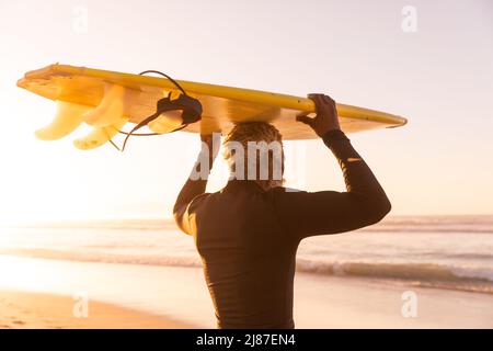 African american senior man carrying surfboard on head while standing at beach against clear sky Stock Photo