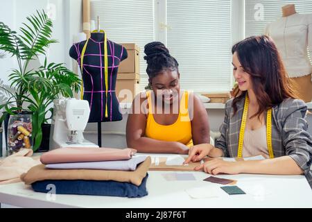 beautiful woman seamstress with long hair and afro customer. tailor creates an image for her in the sewing workshop fashion house Stock Photo