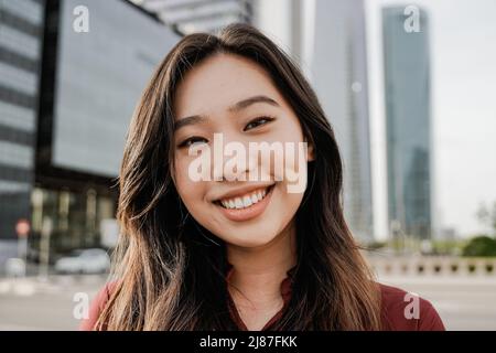 Asian business woman looking at camera outdoor with office buildings on background - Focus on face Stock Photo