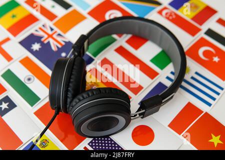 Learning foreign languages online. Headphones and countries flags on the background. Stock Photo