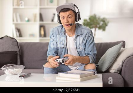 Guy with headphones and a joystick sitting on a sofa and playing video games at home Stock Photo