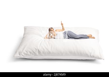 Smiling young woman lying on a comfortbale big pillow in pajamas and pointing up isolated on white background Stock Photo