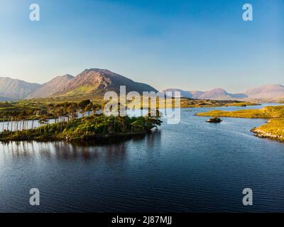 Aerial view of Twelve Pines Island, standing on a gorgeous background formed by the sharp peaks of a mountain range called Twelve Pins or Twelve Bens, Stock Photo