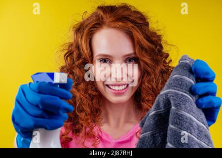 good looking redhair curly ginger pterry woman holding spray and washing windows in studio yellow background Stock Photo