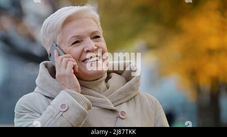 Close-up elderly lady speak on smartphone shares news grandma enjoying using device outdoors positive aged woman smiling talking with children by Stock Photo