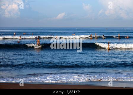 Many surfers riding waves in the sea at Batu Bolong Beach in Canggu, Bali, Indonesia with blue ocean and blue sky on a sunny day. Stock Photo