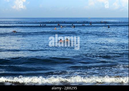 Many surfers riding waves in the sea at Batu Bolong Beach in Canggu, Bali, Indonesia with blue ocean and blue sky on a sunny day. Stock Photo