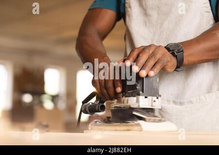 Midsection of african american mature carpenter using sander on plank at workshop Stock Photo