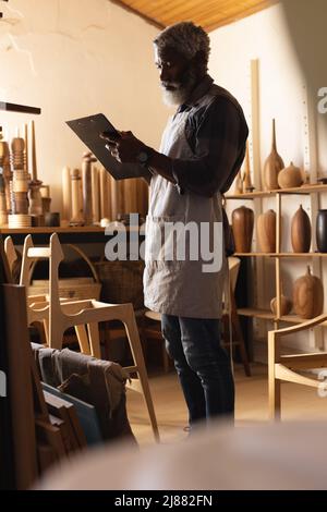 African american mature carpenter writing in clipboard while working in workshop Stock Photo