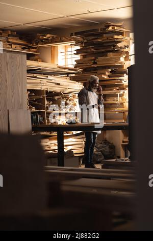African american mature carpenter talking on smartphone in woodworking workshop Stock Photo